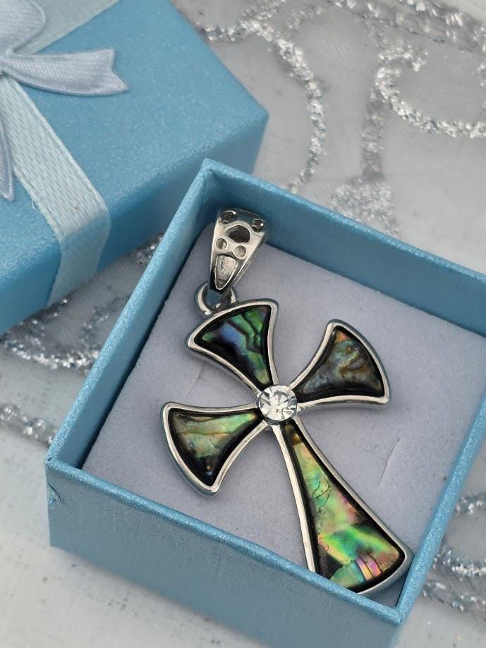A silver-toned pendant cross with colorful inlays is displayed in a blue gift box, with a silver clasp and a white ribbon bow.