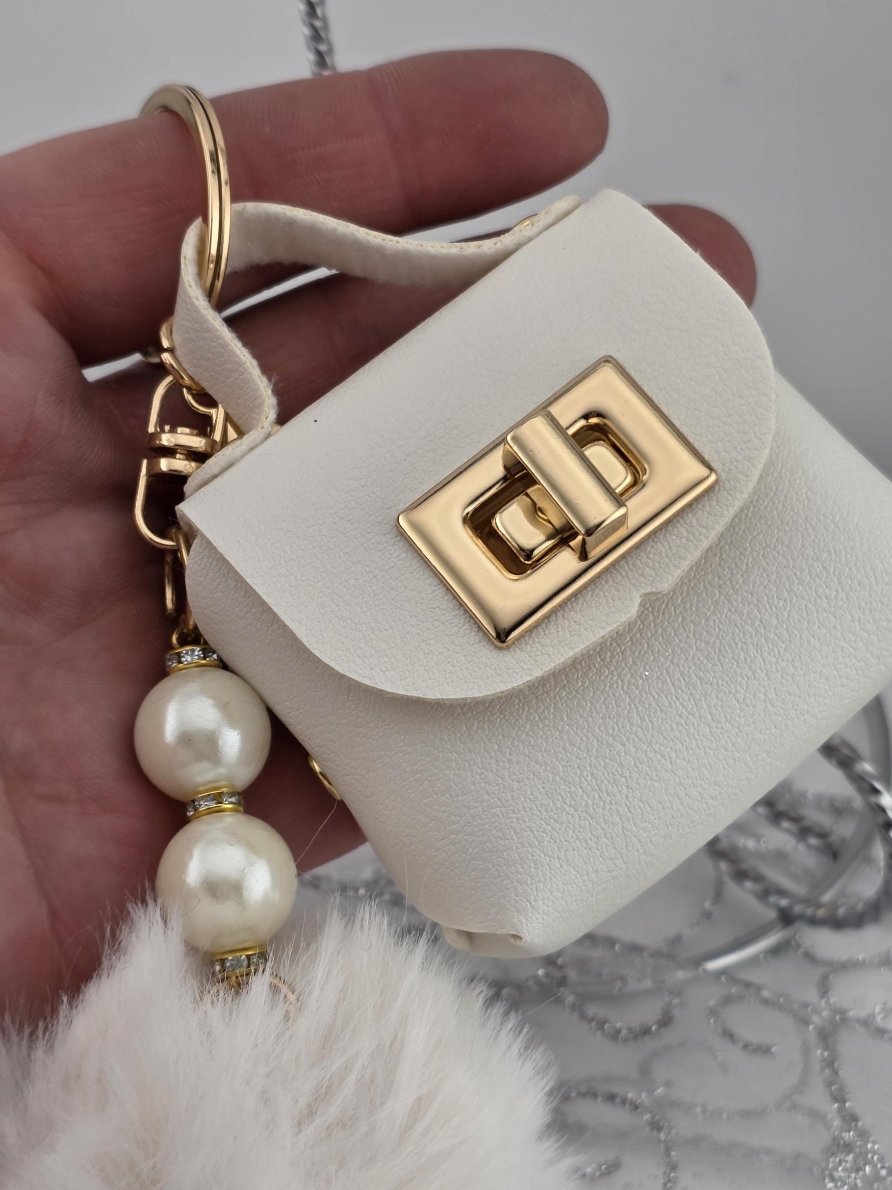 A hand holding a white leather handbag with a gold lock and a chain attached to it.