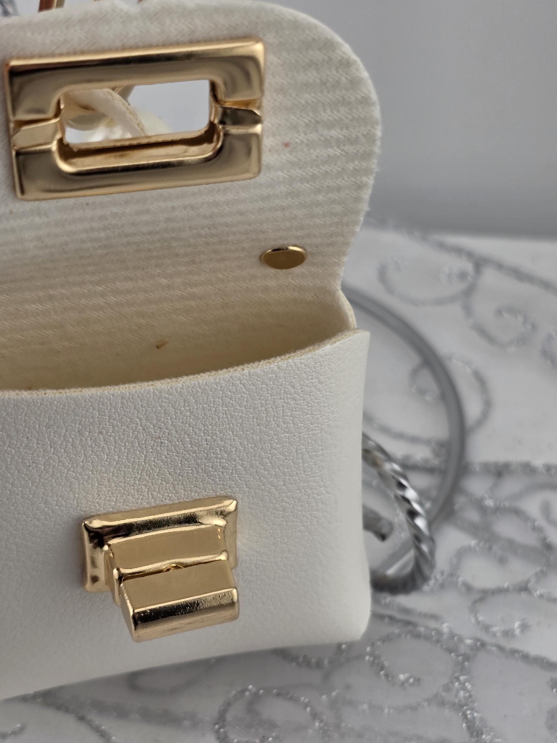 A close-up view of a white leather handbag with a gold-colored metal clasp and a gold-colored metal buckle.