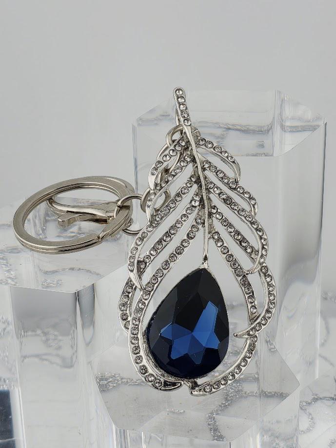 A silver keychain with a large blue gemstone in the shape of a feather.