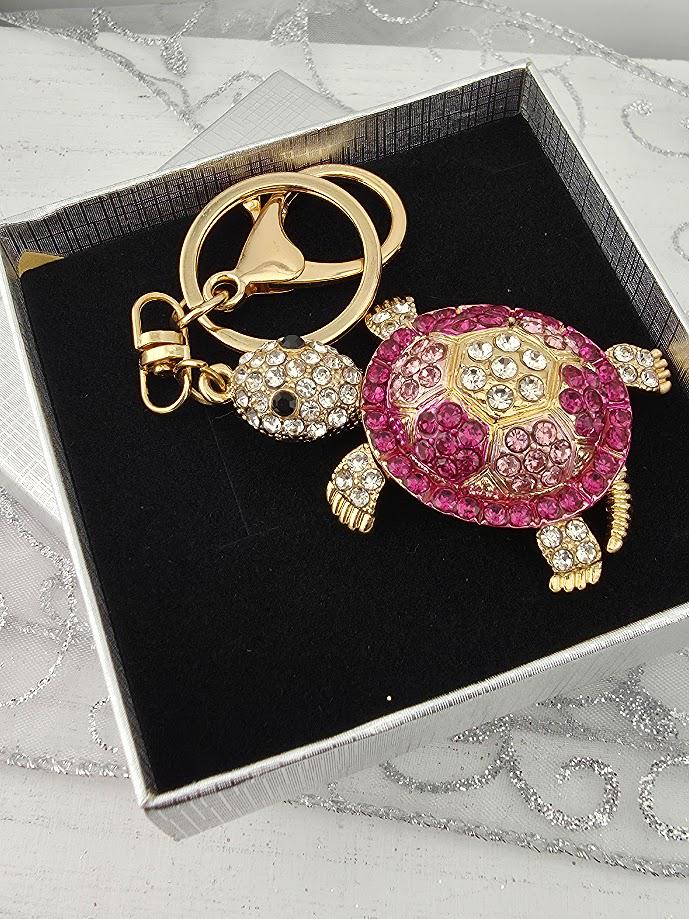A keychain with a pink and gold turtle design, adorned with rhinestones and a gold-colored clasp.