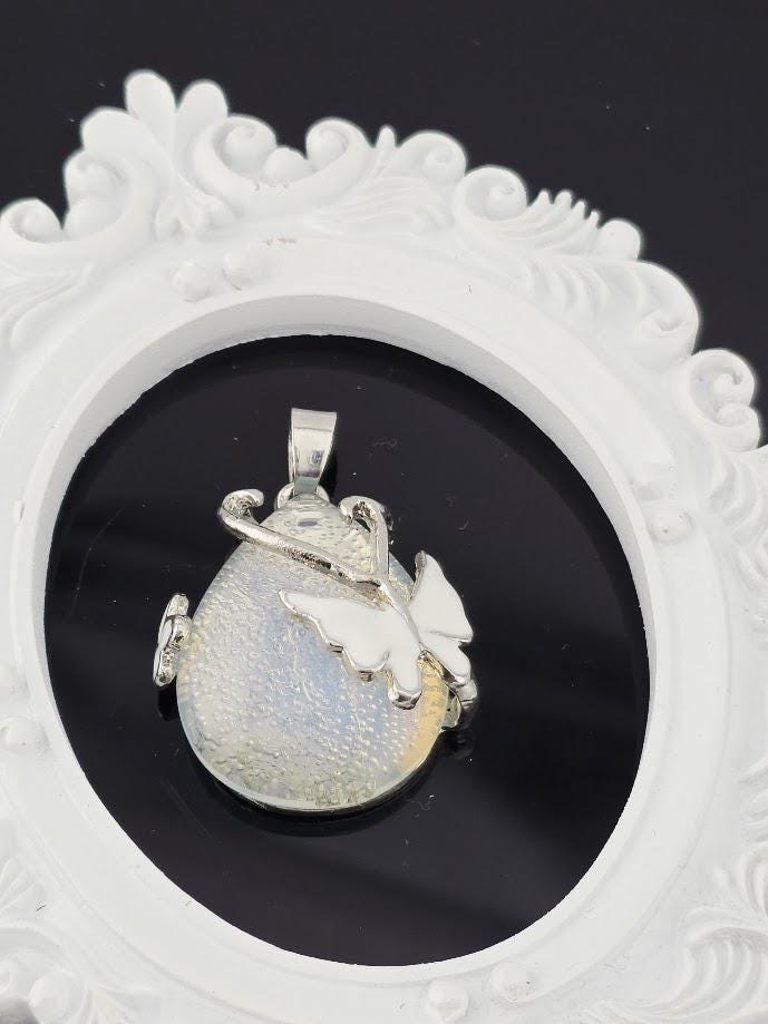 A silver pendant with a butterfly design is displayed in a white ornate frame against a black background.
