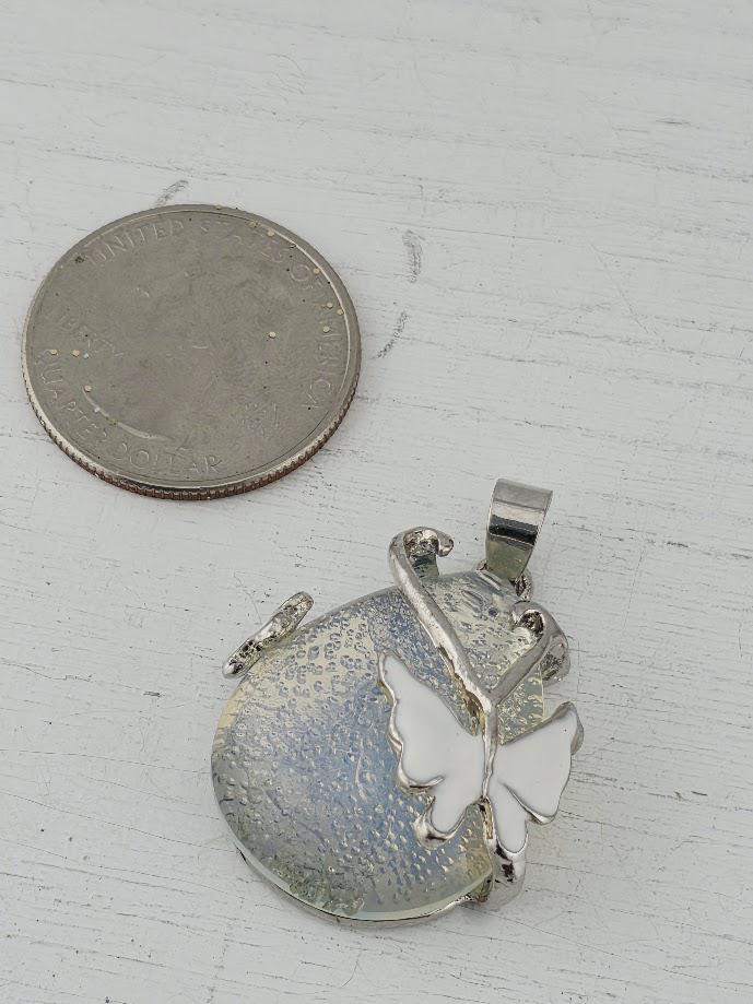 A silver butterfly pendant is shown next to a United States quarter coin on a white surface.