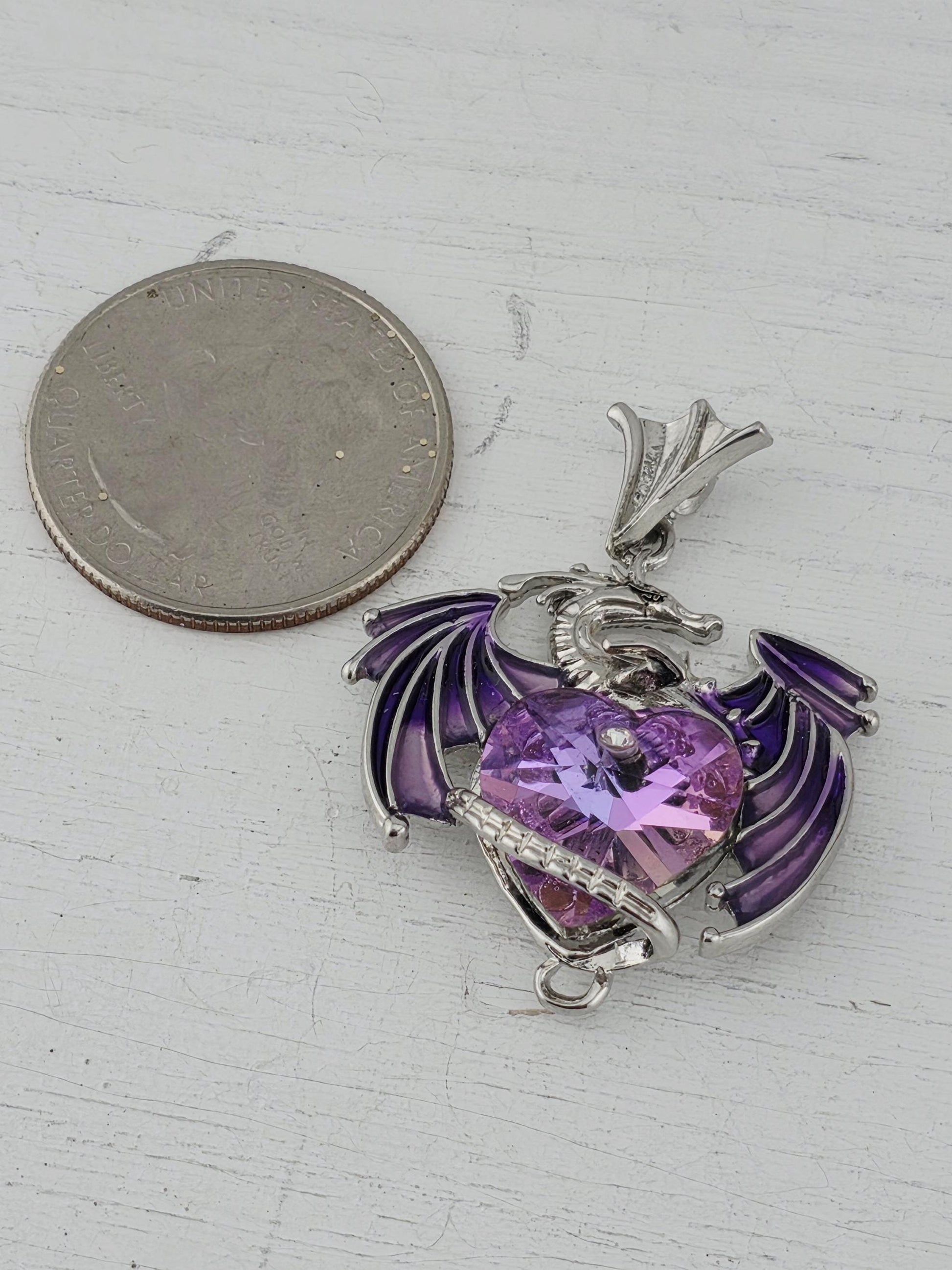 A silver-toned pendant with a purple gemstone, resembling a dragon or mythical creature, is shown next to a United States quarter coin.