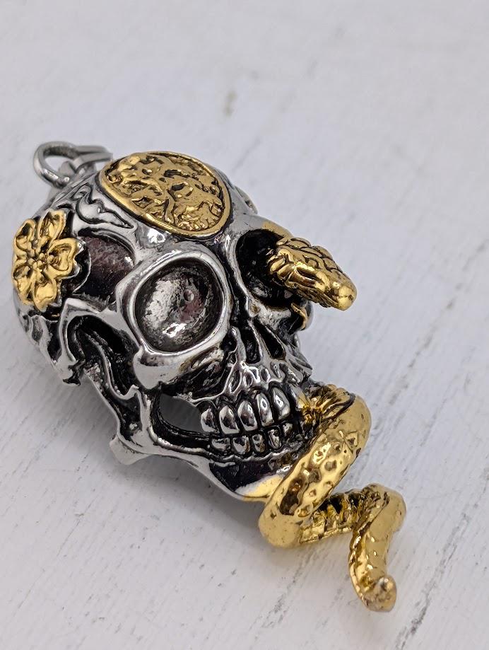 A silver and gold pendant in the shape of a skull with a snake wrapped around it.