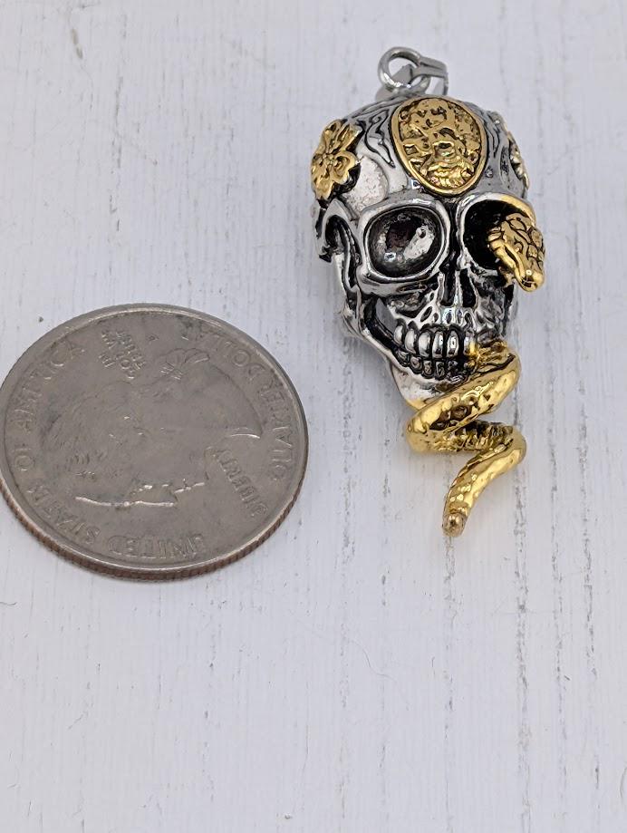 A silver-colored coin next to a skull pendant with a snake design.