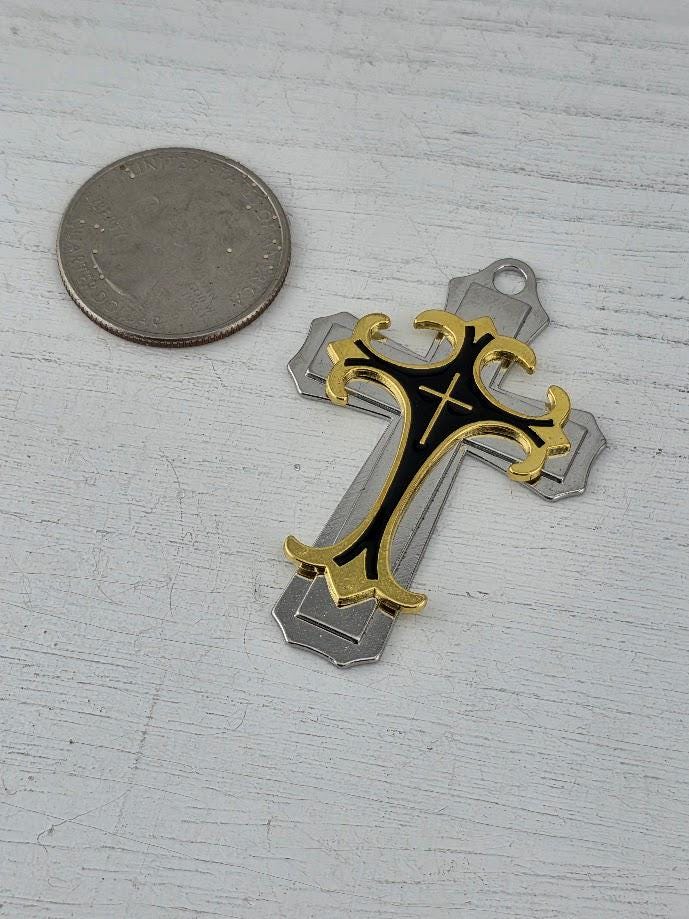 A silver and black cross-shaped ornament is displayed in a black box with a gold ribbon bow.