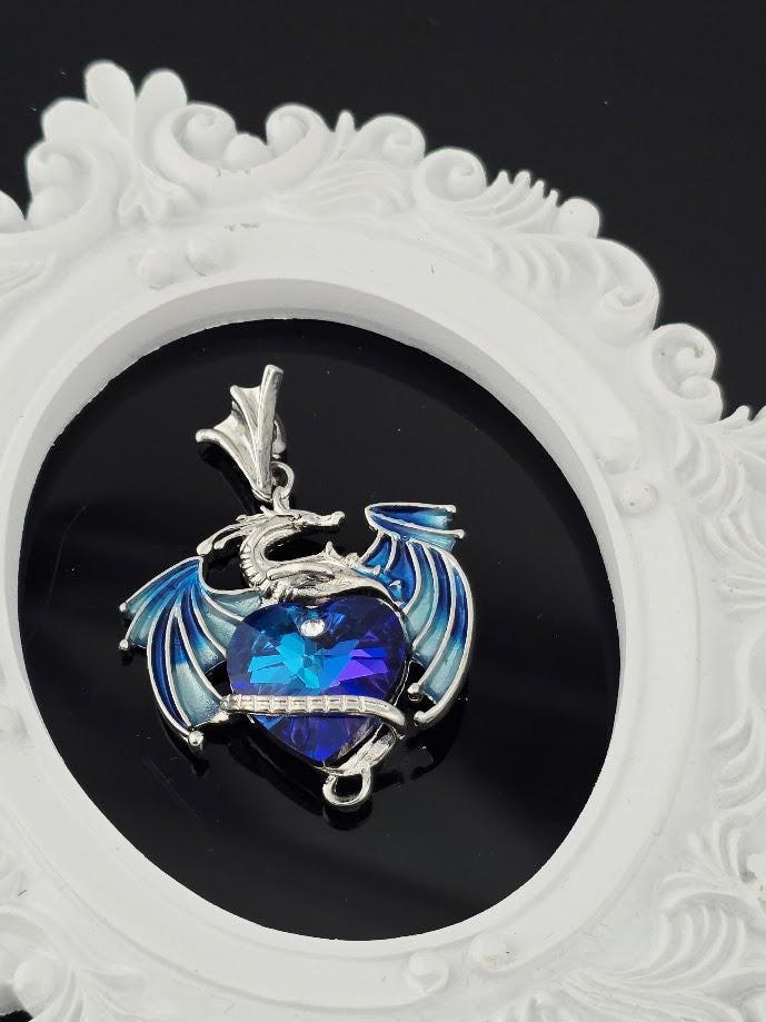 A pendant in the shape of a dragon with a blue gemstone in its mouth, set against a white ornate frame.