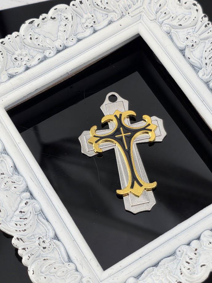 A decorative white frame with an ornate border surrounds a gold and black cross-shaped pendant.