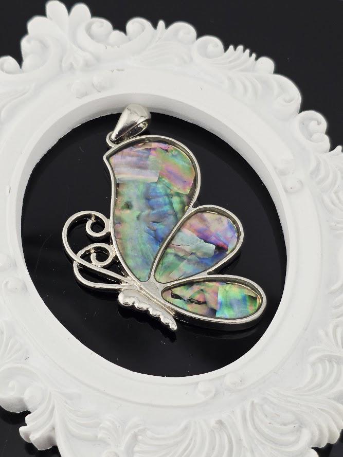 A silver butterfly pendant with colorful iridescent wings is displayed in a white jewelry box with a gold ribbon.