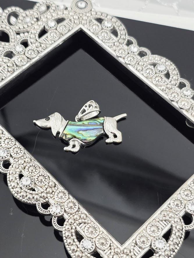 A silver-toned pendant in the shape of a dog, with a colorful iridescent design, is displayed in a decorative silver frame.