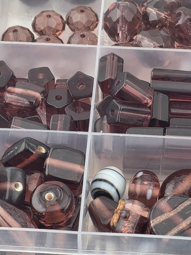 a collection of various colored glass beads, including shades of brown, black, and white, arranged in a transparent container.