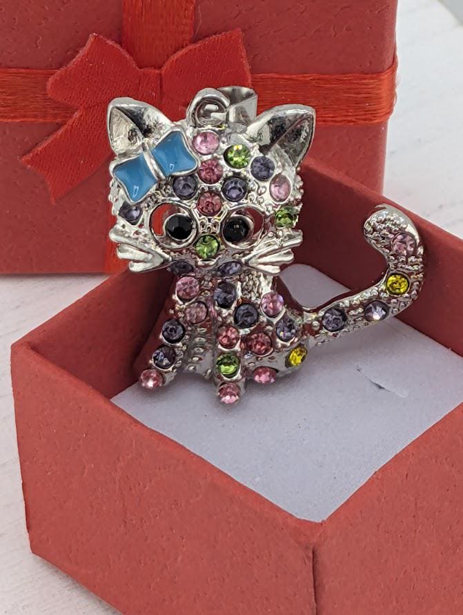 A silver cat-shaped pendant with colorful gemstones is displayed in a red gift box.
