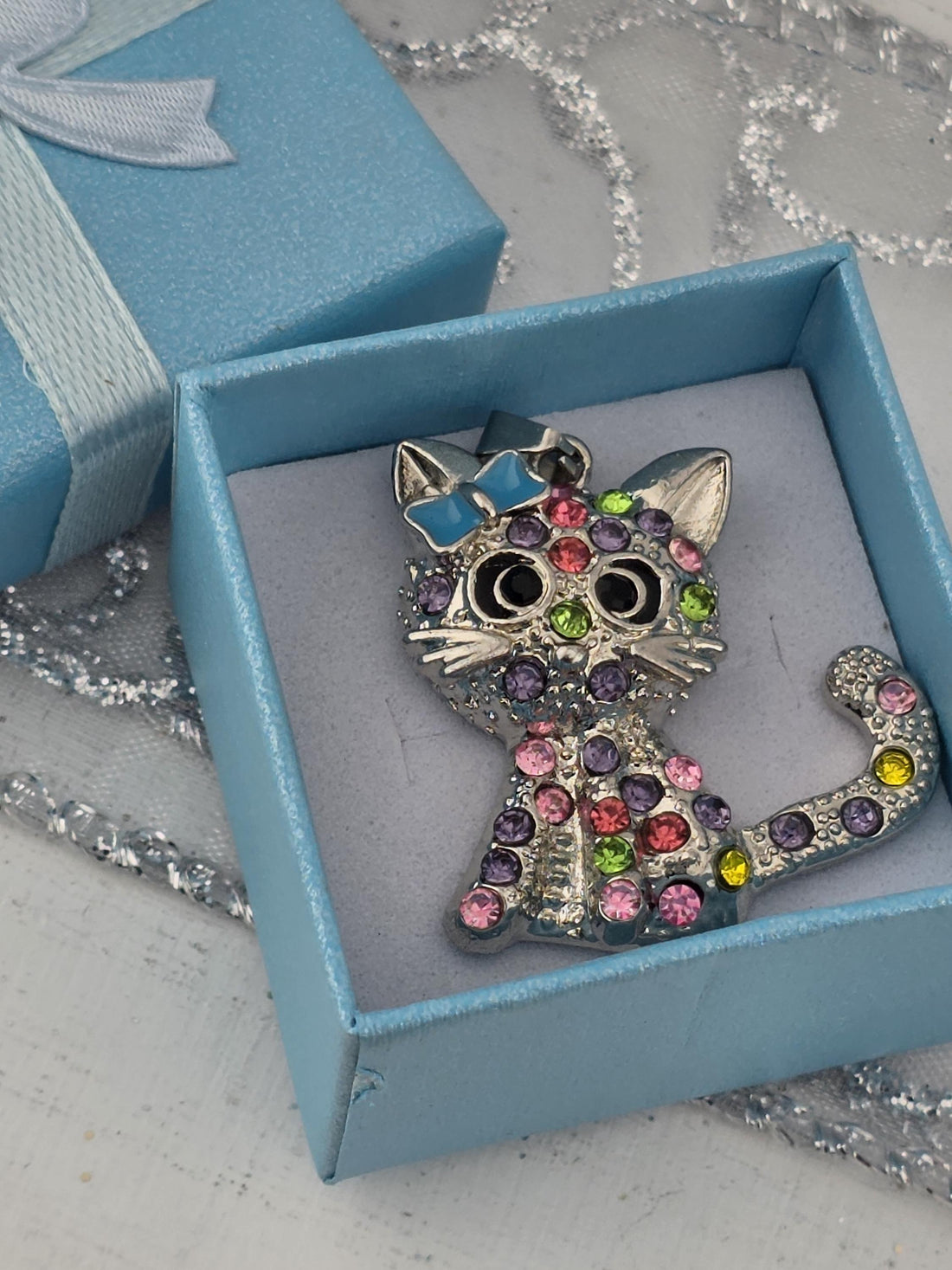 A silver cat-shaped pendant with colorful gemstones is displayed in a red gift box.