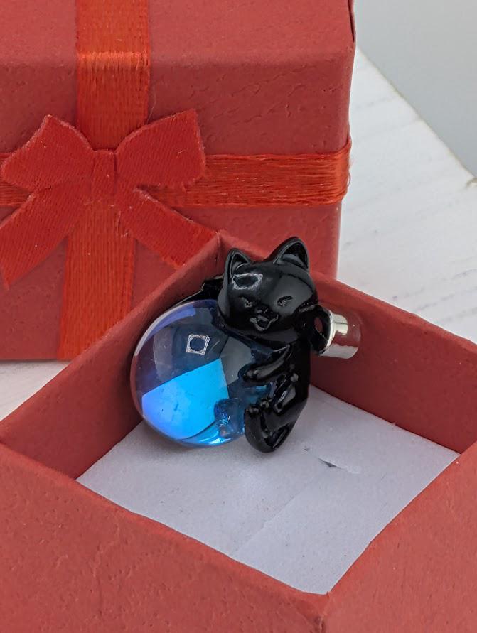 A small black cat figurine is sitting inside a red gift box with a red ribbon bow.