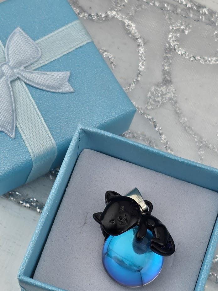 A blue gift box with a white ribbon and a black cat charm resting on a blue glass ball.
