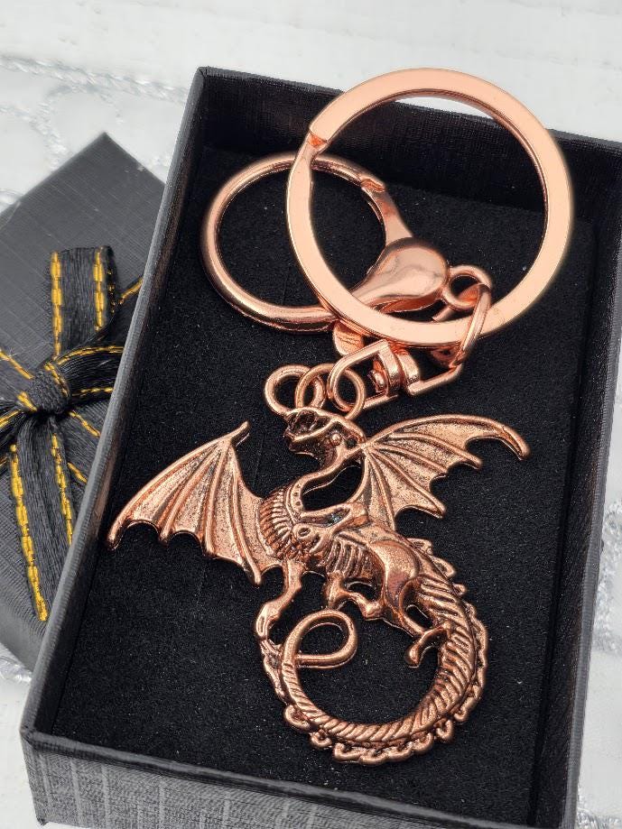 A copper-colored dragon keychain is displayed in a black box with a yellow ribbon bow.
