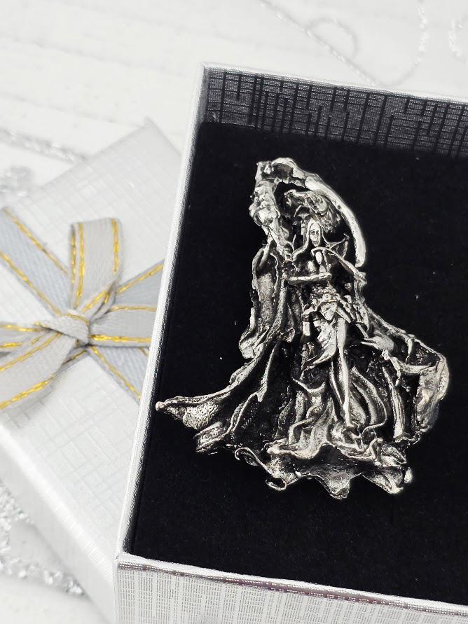 A silver brooch or pendant is displayed in a white gift box with a gold ribbon, placed on a white surface.