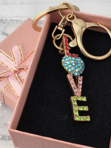 A pink gift box with a keychain attached to it, featuring a colorful charm in the shape of the word "LOVE".