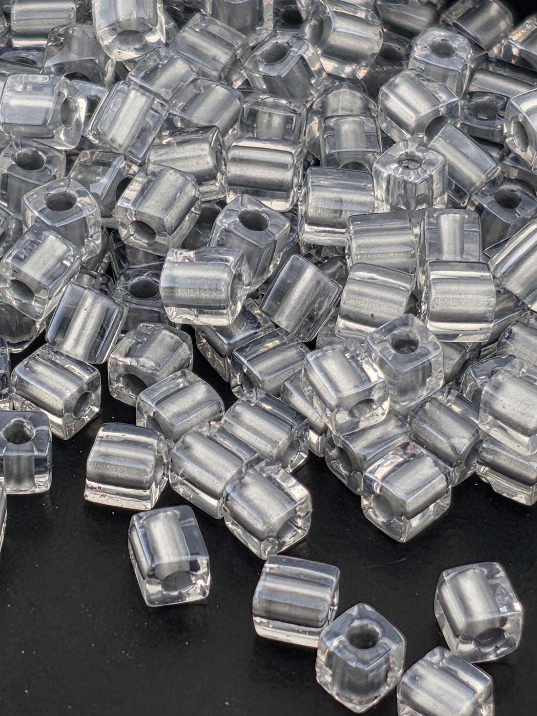 A close-up image of numerous clear glass beads scattered on a dark background.