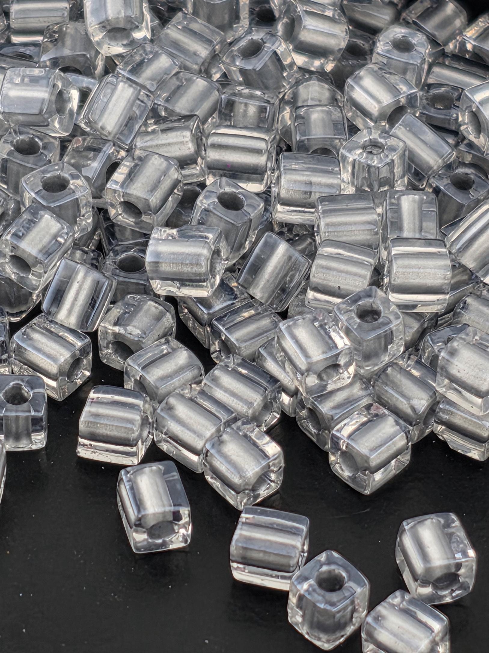 A close-up image of numerous clear glass beads scattered on a dark background.