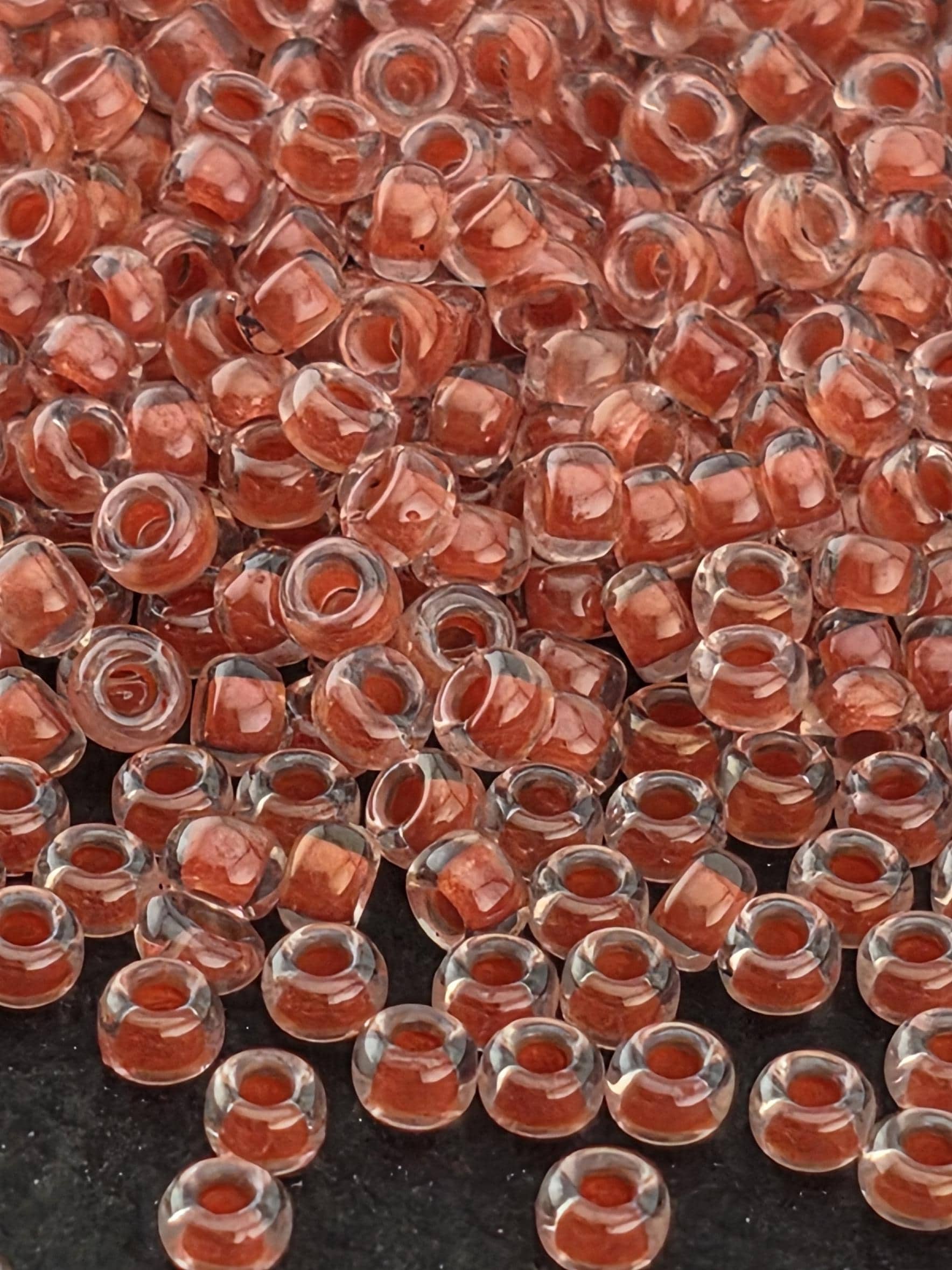 a close-up view of numerous small, clear beads in various shades of red, scattered across a dark background.