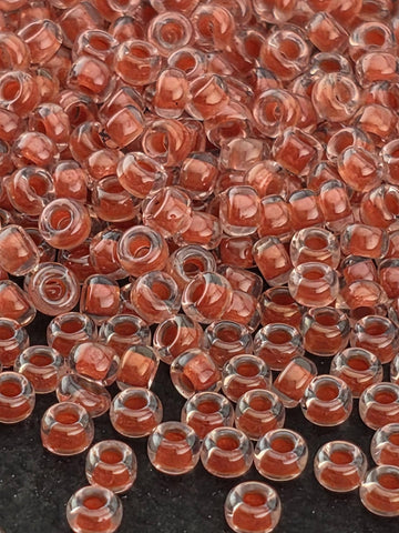 a close-up view of numerous small, clear beads in various shades of red, scattered across a dark background.