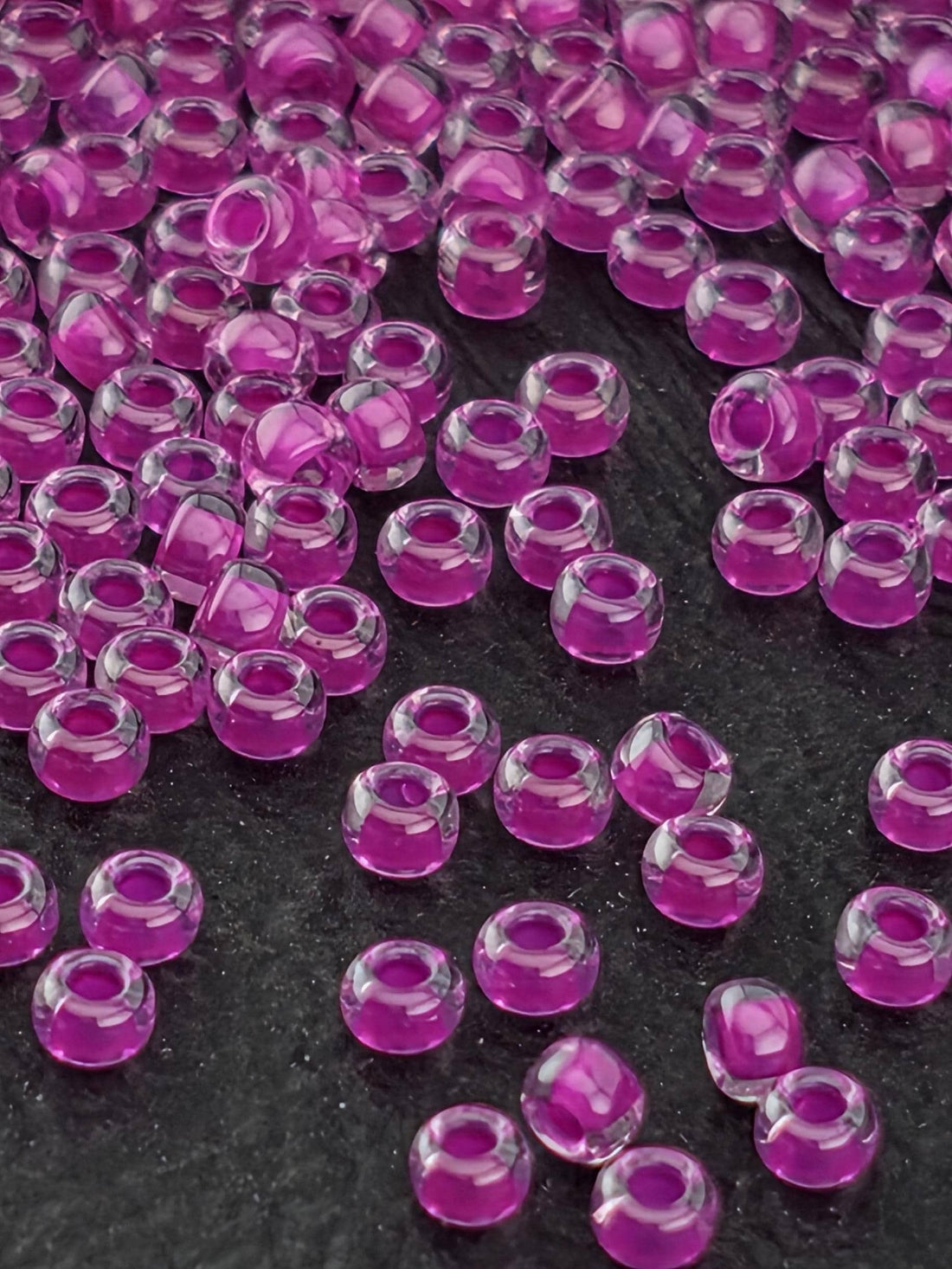 a close-up view of numerous small, clear beads in shades of purple and pink, scattered across a dark background.