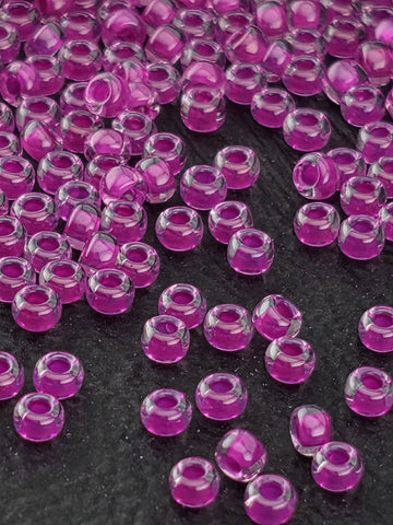 a close-up view of numerous small, clear beads in shades of purple and pink, scattered across a dark background.