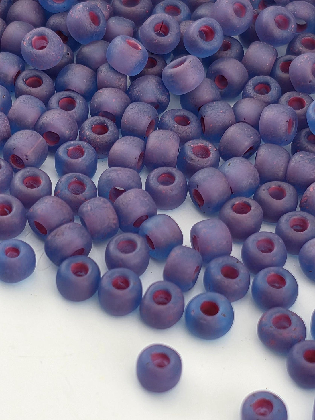 a close-up view of numerous small, round beads in shades of purple and red, scattered across a white surface.