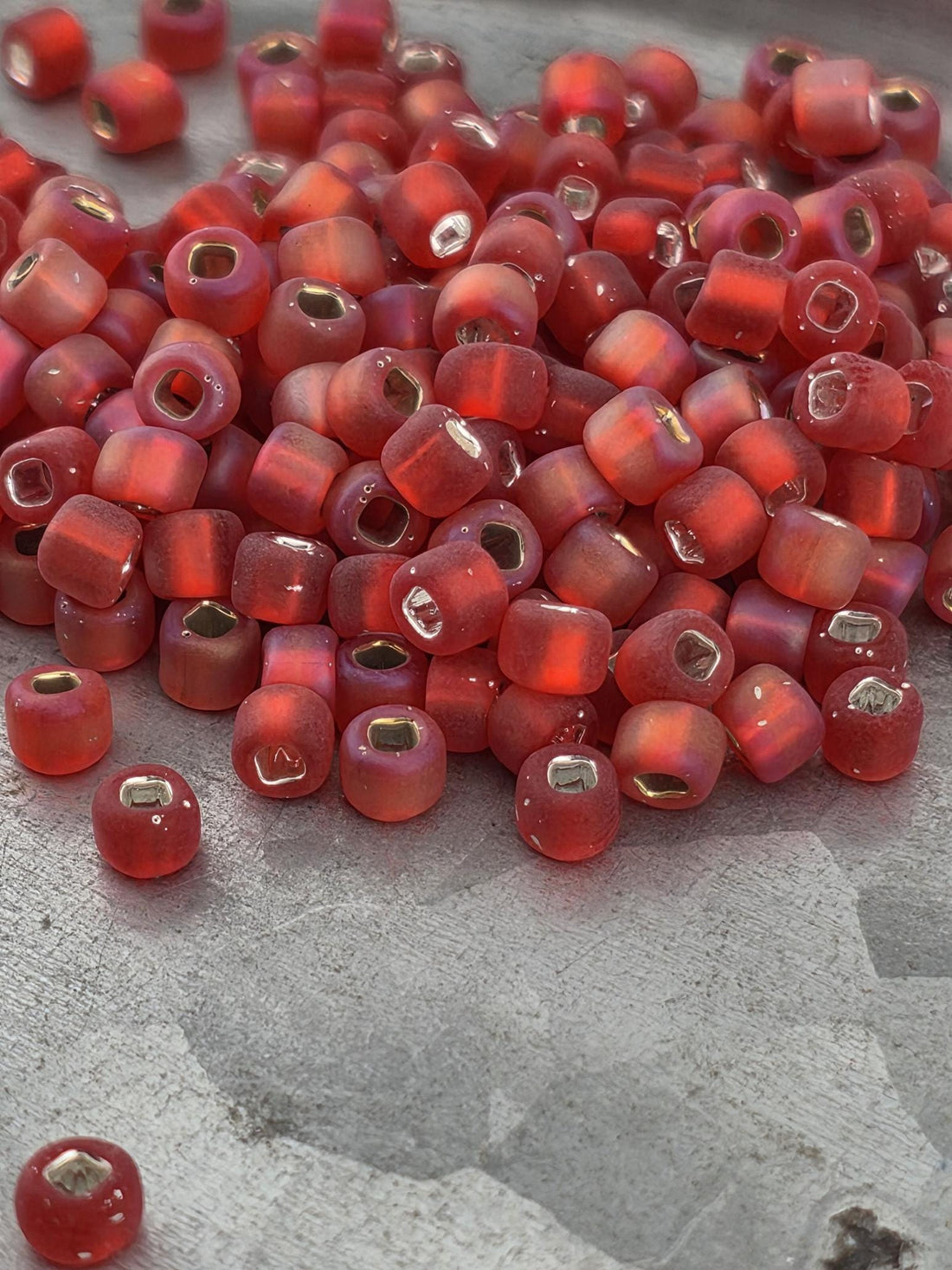 A pile of red glass beads with gold accents, scattered on a gray surface.