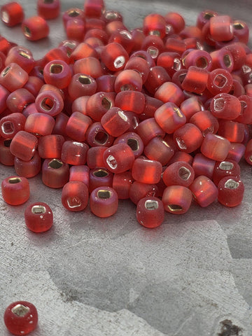 A pile of red glass beads with gold accents, scattered on a gray surface.