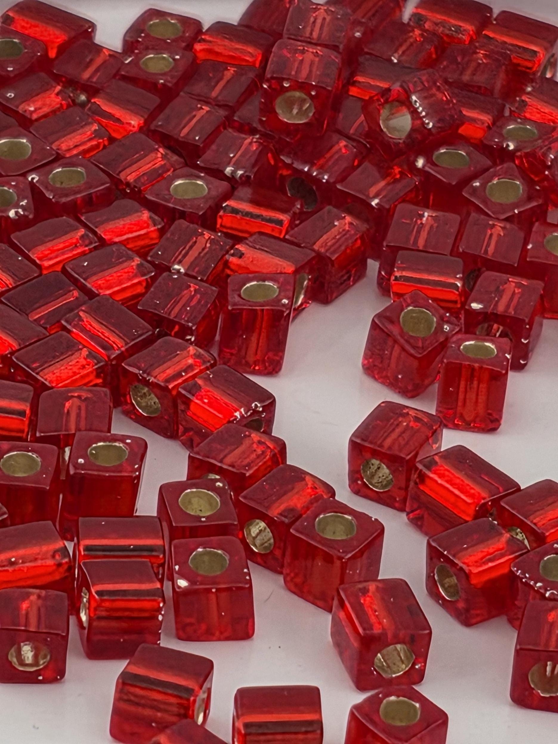 a collection of red glass beads or stones, possibly made of a shiny, translucent material. The beads are scattered across a surface, creating a visually striking and colorful display.