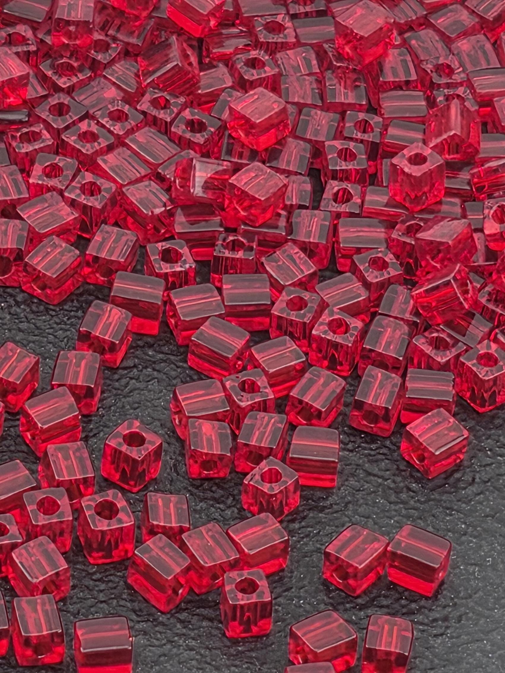 The image is a close-up of numerous red glass beads scattered across a dark surface.