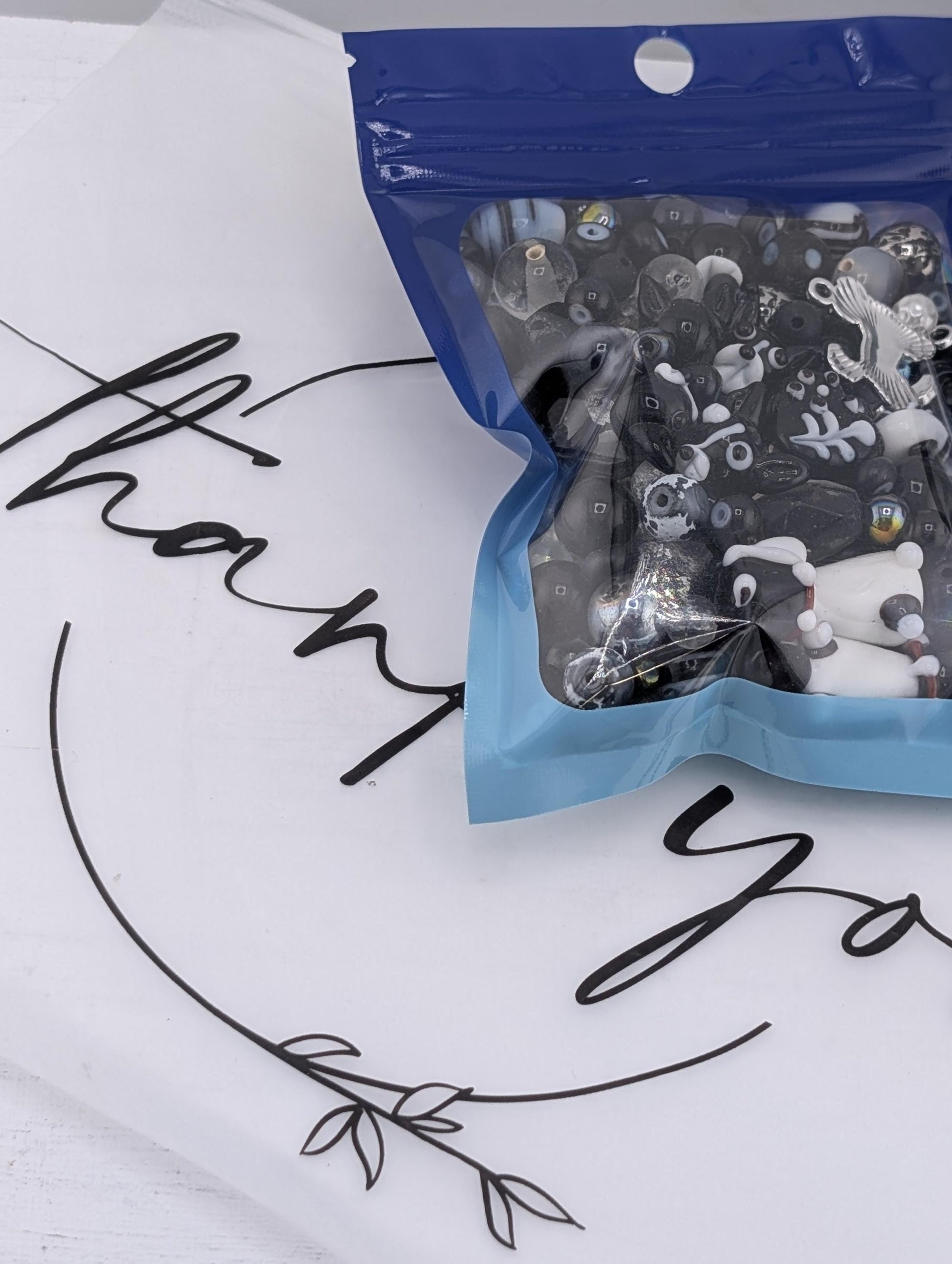 A package of black and white toy figurines is shown on a white surface, with a blue and white "Thank you" sign in the background.