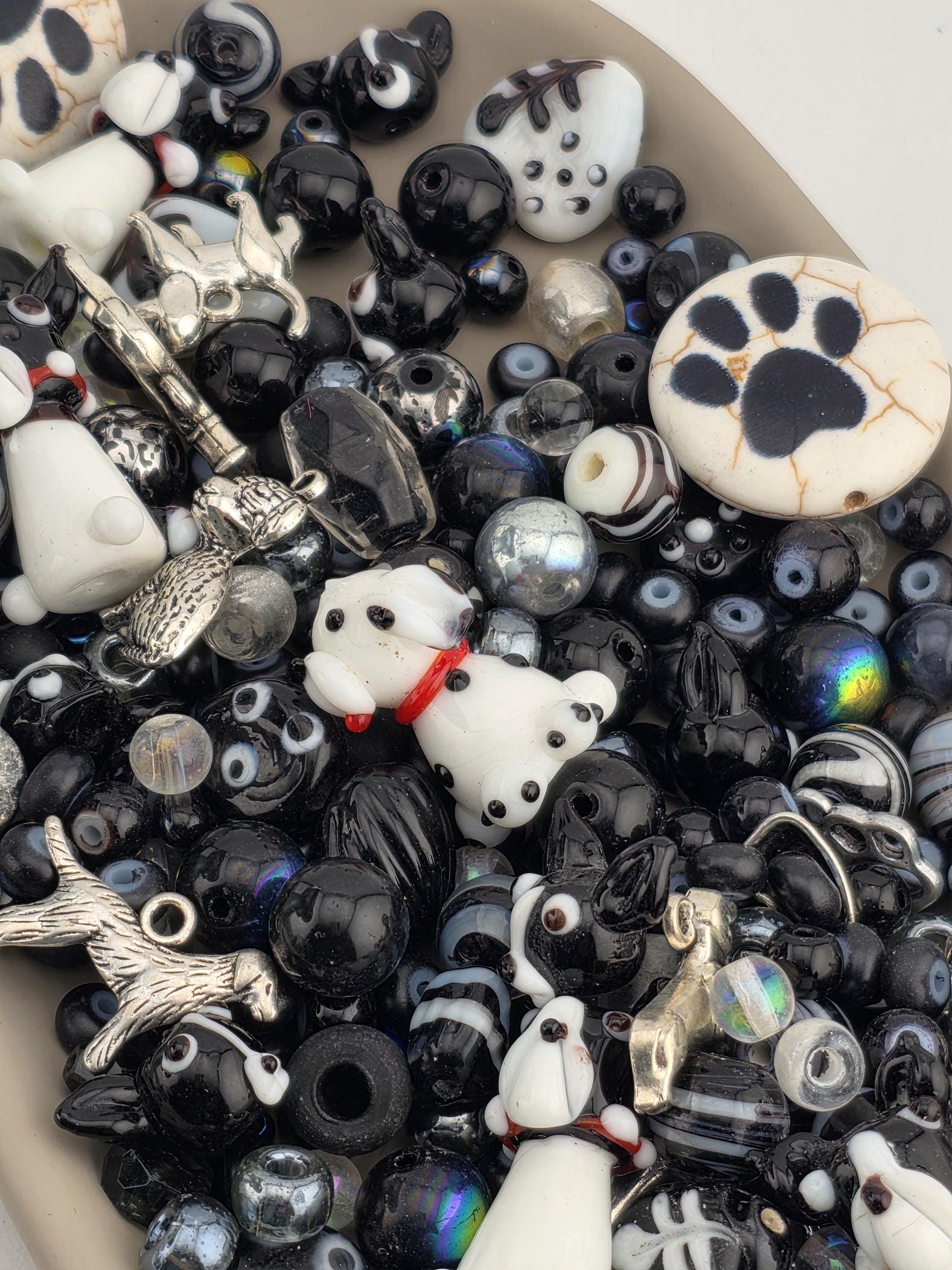 A collection of various beads, charms, and figurines in shades of black and white, including dog-themed items.