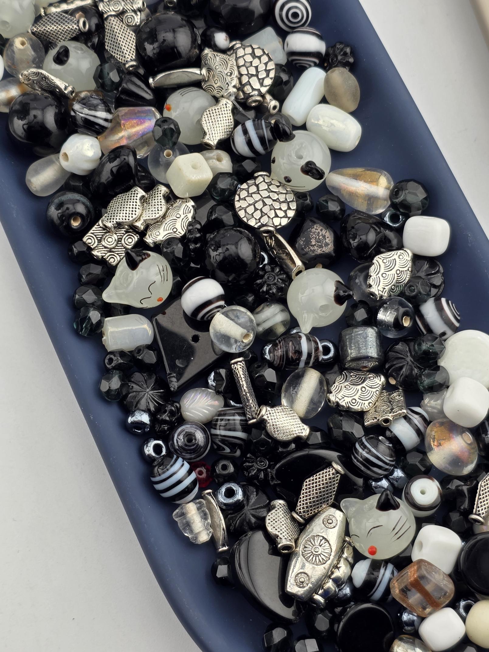 A blue tray filled with various beads, charms, and other decorative items in shades of black, white, and silver.