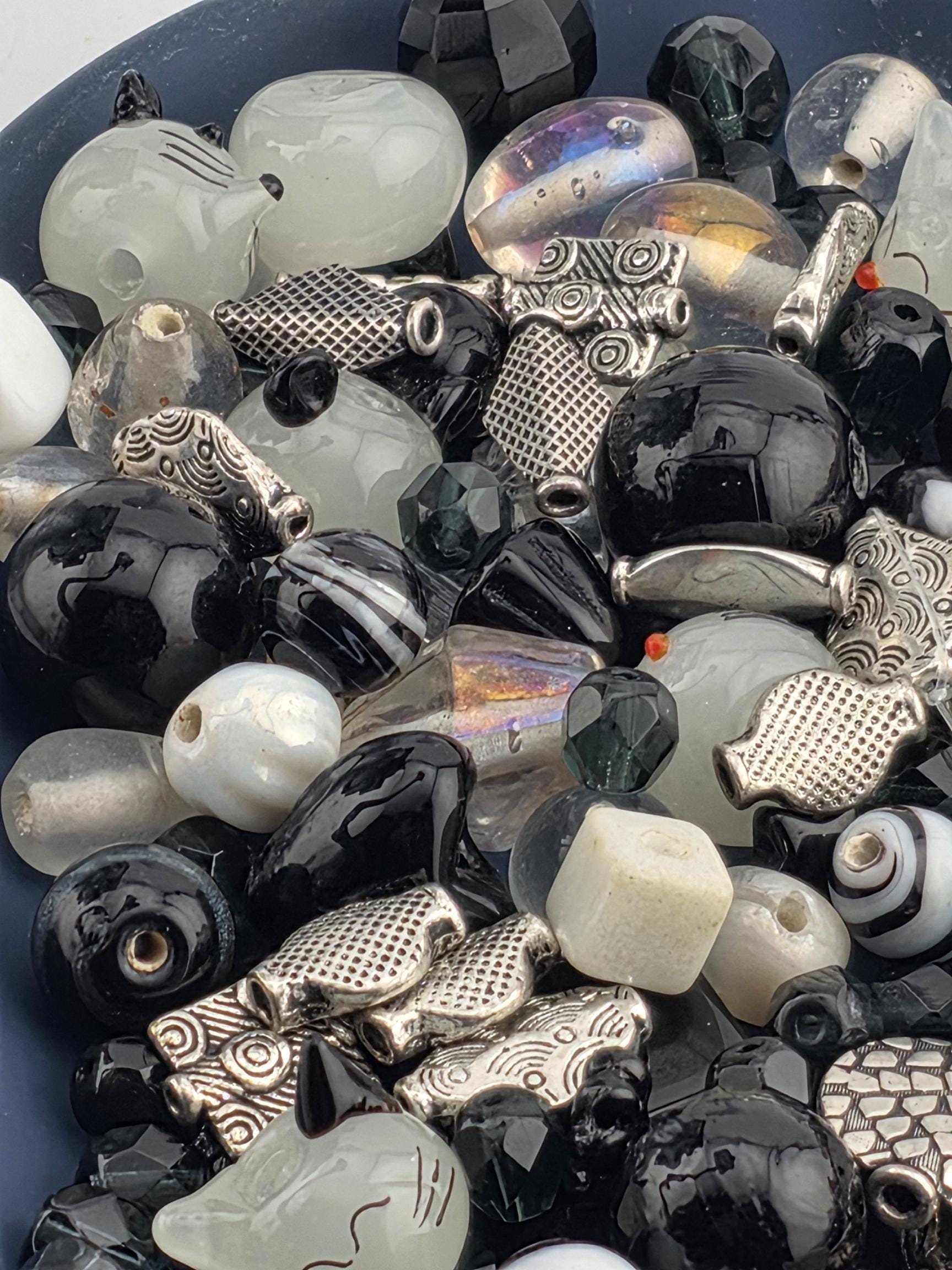 The image is a close-up of a collection of various beads and beads, including black, white, and silver beads, as well as some with intricate designs.
