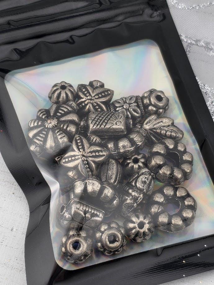 A black plastic bag filled with various metal beads, including star-shaped, flower-shaped, and other intricate designs.