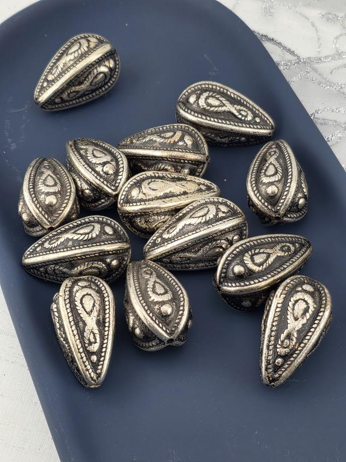 a collection of ornate metal beads or coins with intricate designs, arranged on a dark surface.