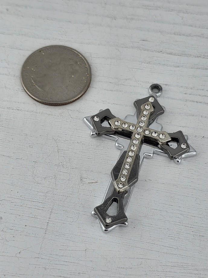 A silver cross pendant with rhinestones is displayed in a silver box with a gold ribbon bow.
