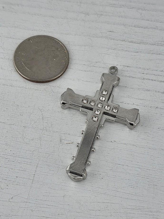 A silver cross pendant with small rhinestones is displayed in a silver box with a gold ribbon bow.