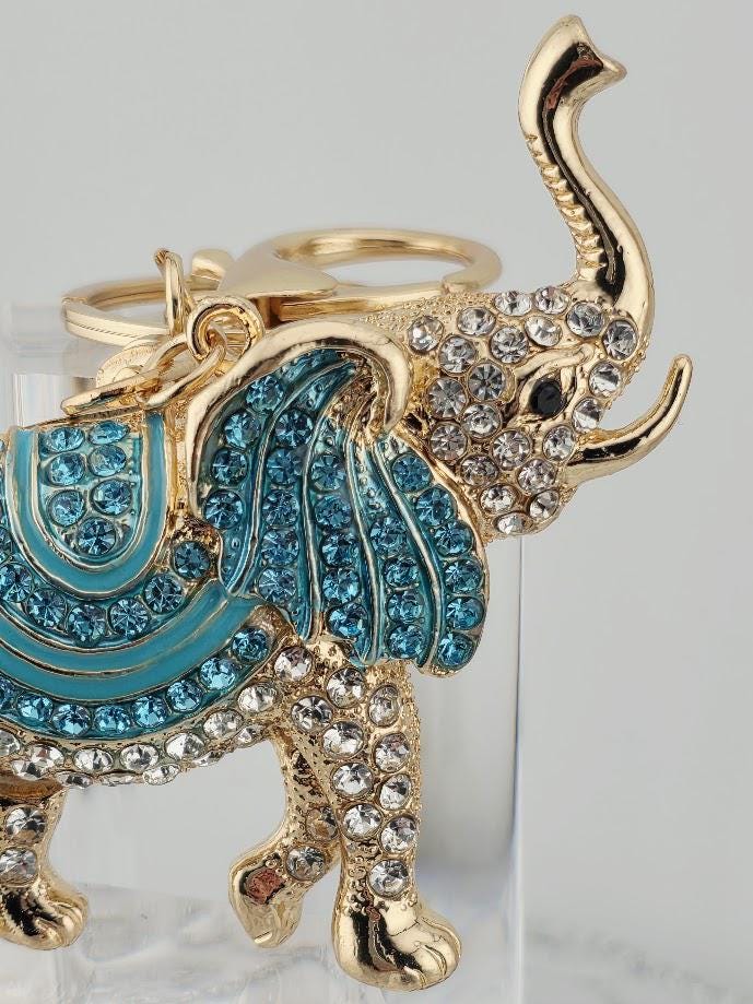 A decorative elephant keychain with a gold-colored trunk and blue and white accents, including rhinestones and crystals.