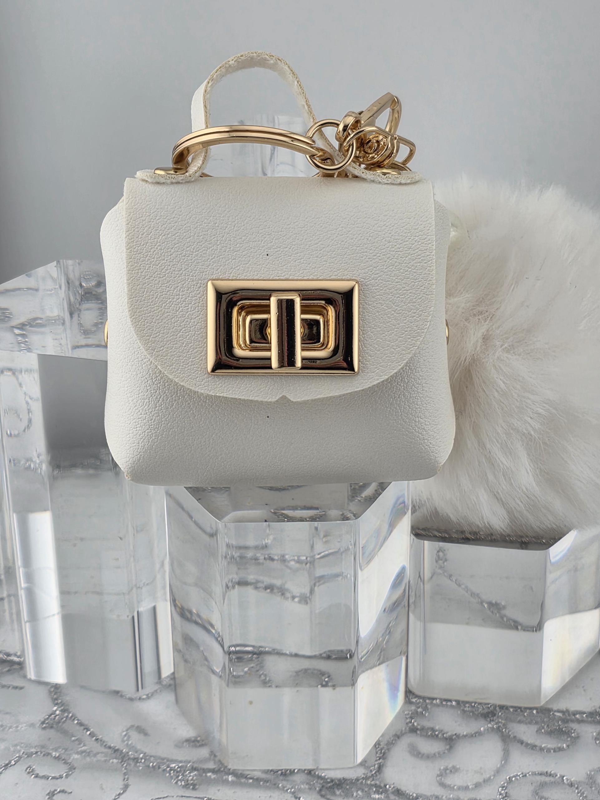 A white leather handbag with a gold lock and chain attached, placed on a white marble surface.