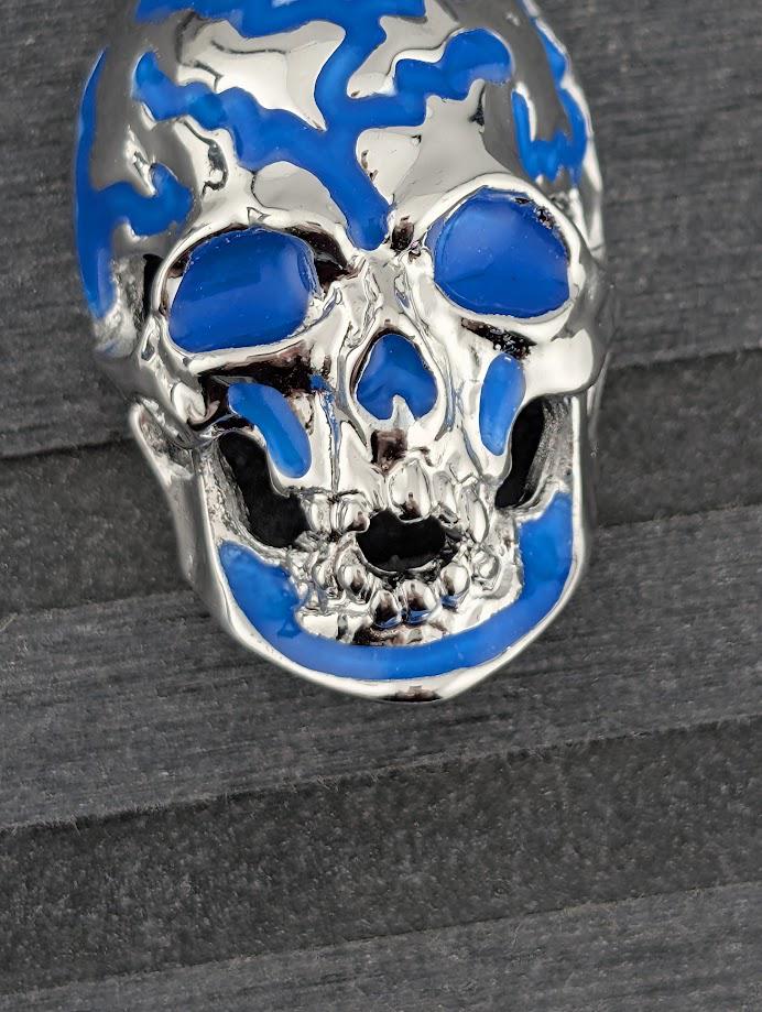 A close-up image of a silver-colored skull with blue accents, placed on a gray surface.
