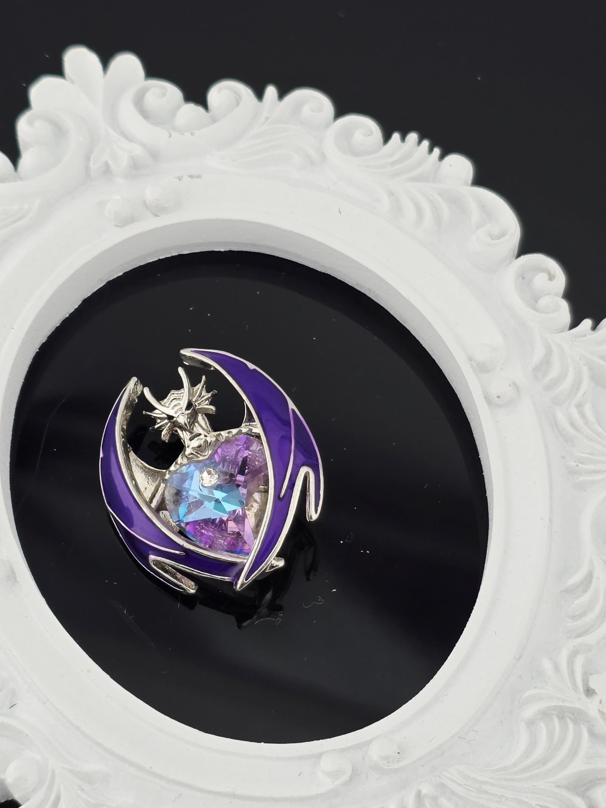 A decorative white frame with a purple and blue design, containing a small, colorful gemstone or piece of jewelry.