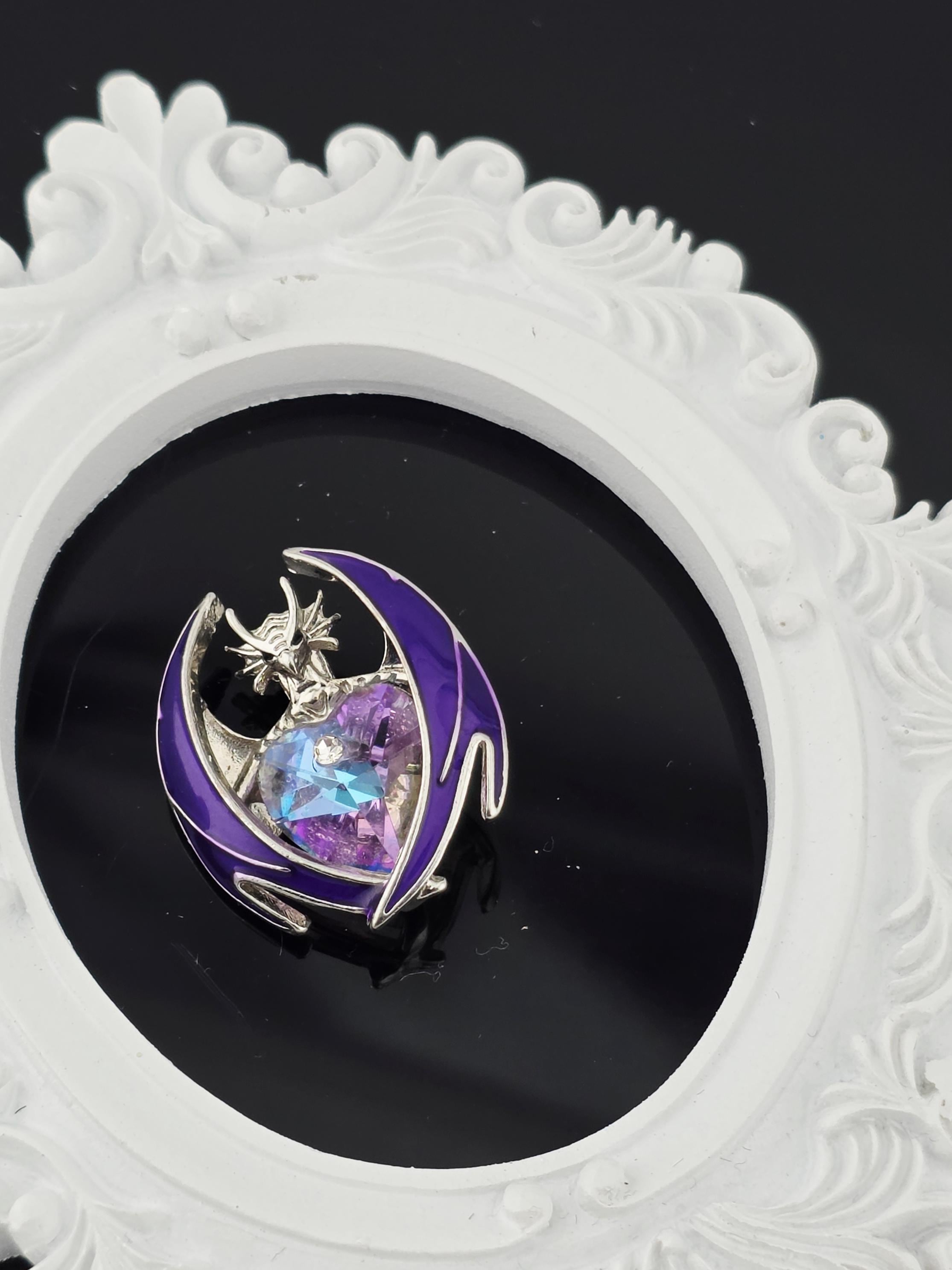 A decorative white frame with a purple and blue design, containing a small, colorful gemstone or piece of jewelry.