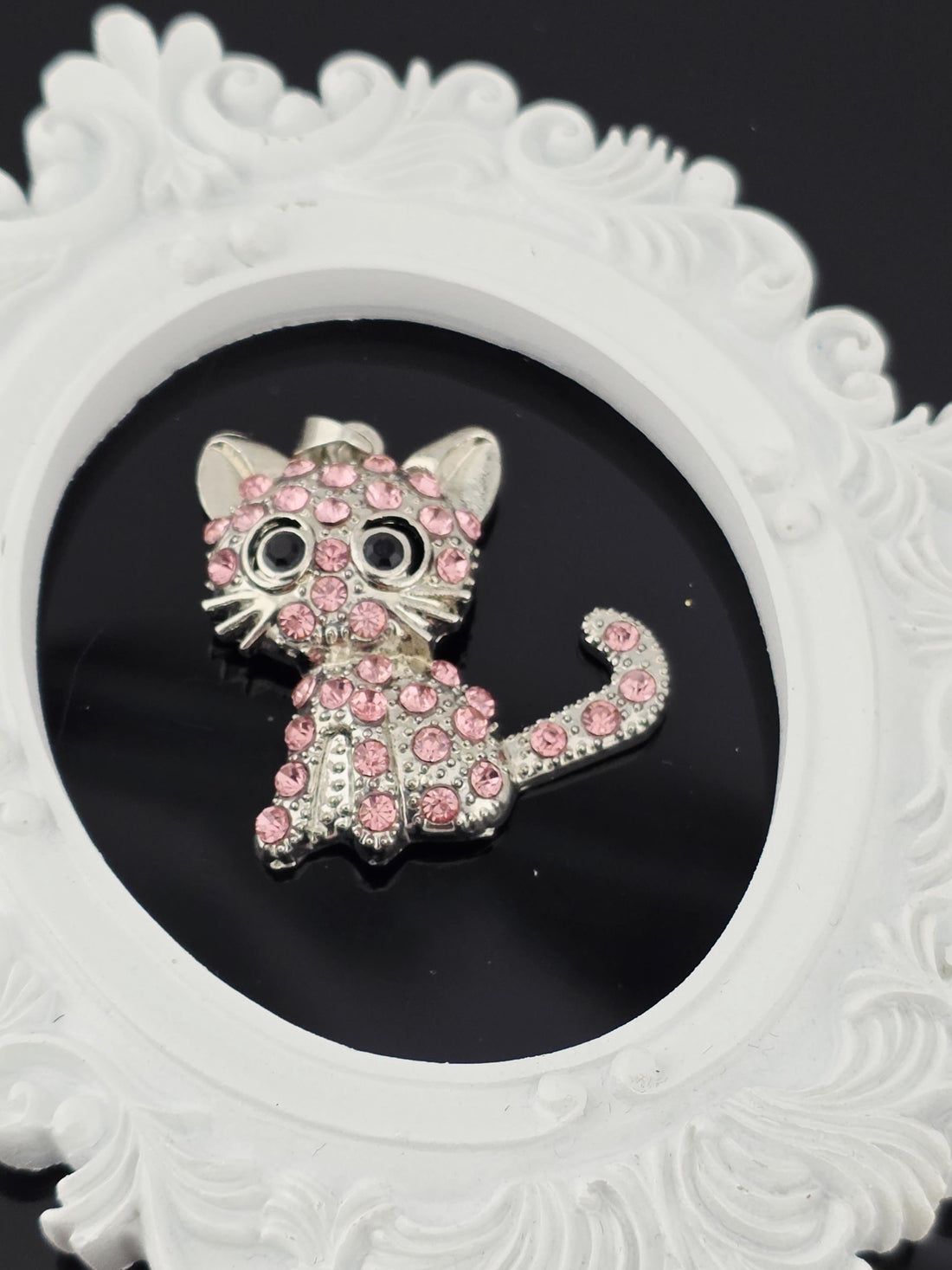 A decorative brooch in the shape of a cat, adorned with pink gemstones, is displayed in a blue gift box with a white ribbon bow.