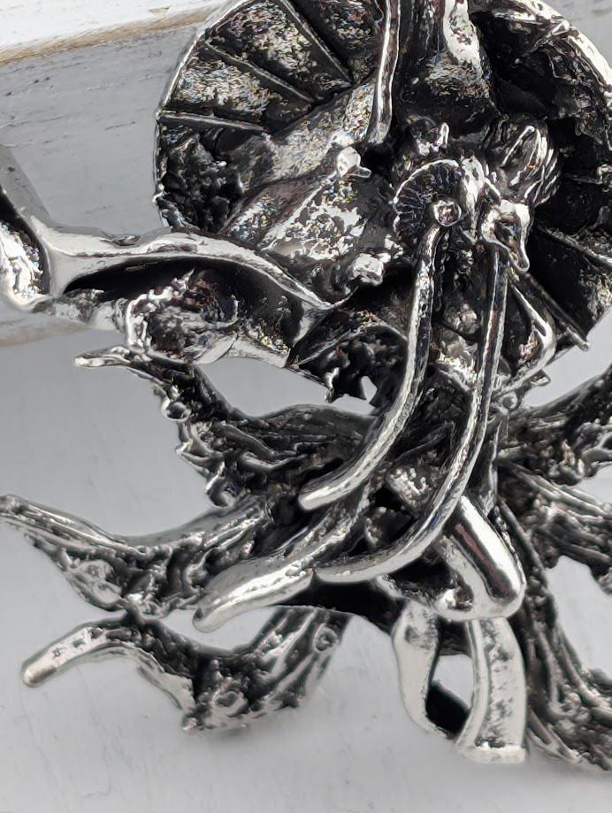 a close-up view of a silver, metallic sculpture with intricate, organic shapes and textures.