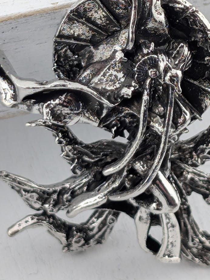 a close-up view of a silver, metallic sculpture with intricate, organic shapes and textures.